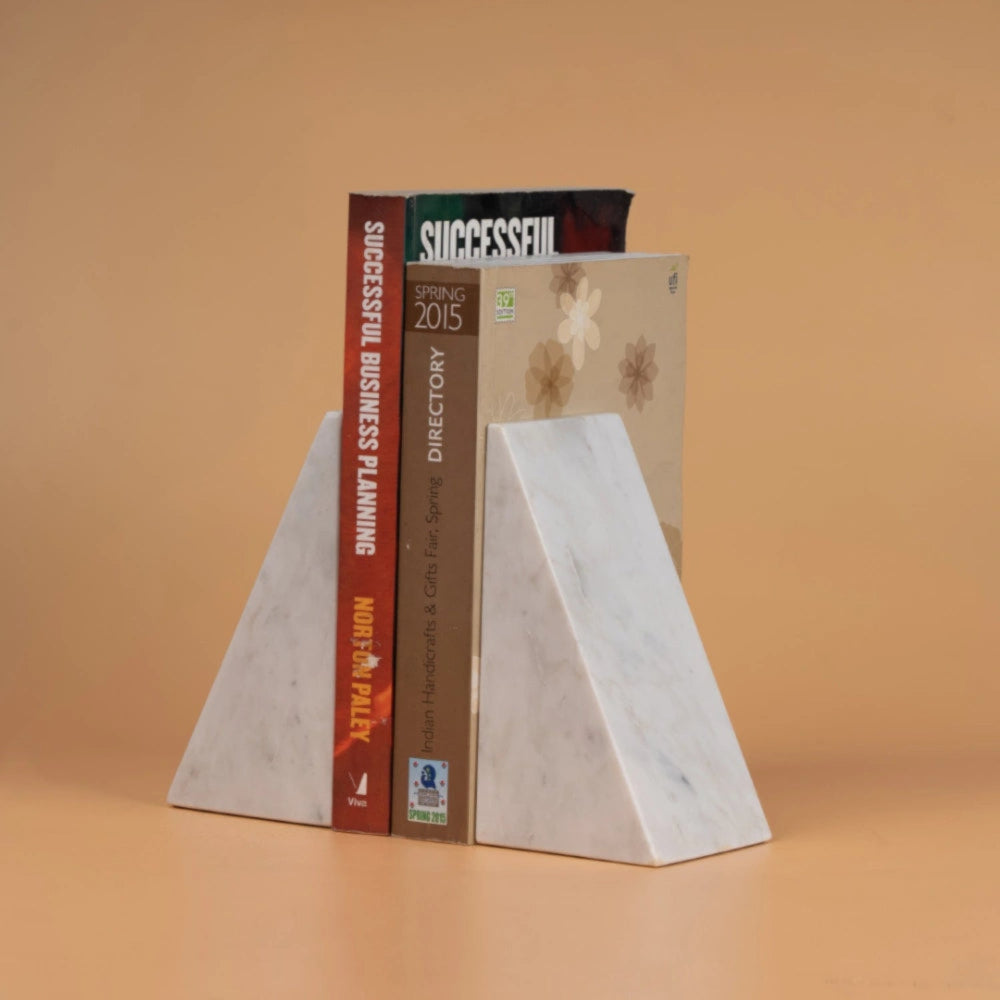 Two white marble pyramid bookends holding up two business books on a warm beige background.